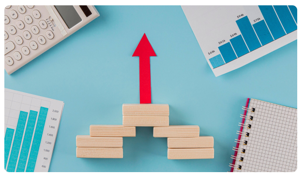 Red arrow rising above stacked wooden blocks beside bar charts and a calculator
